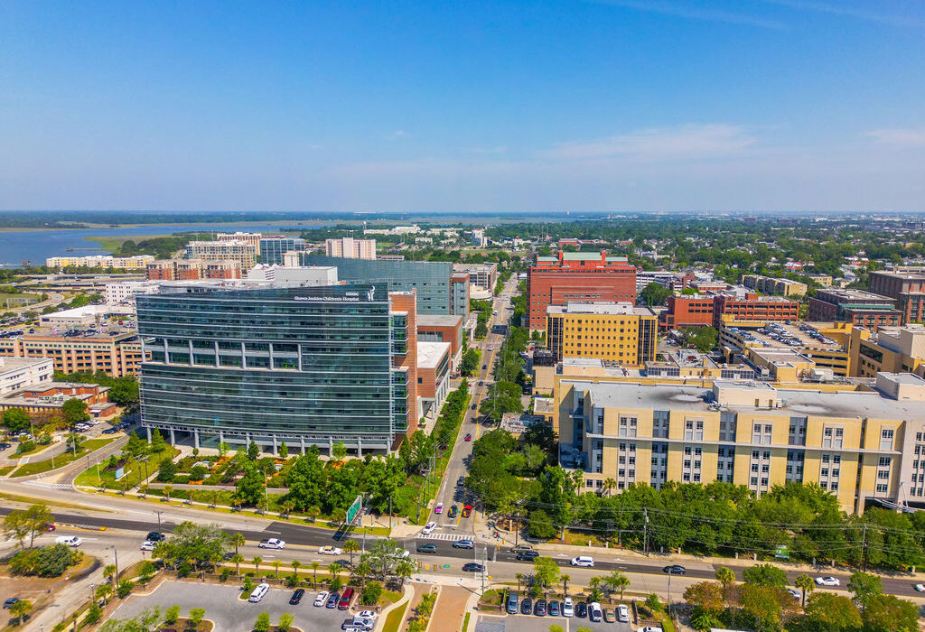 Aerial view of a modern hospital complex and urban medical district with a waterfront in the background on a sunny day.